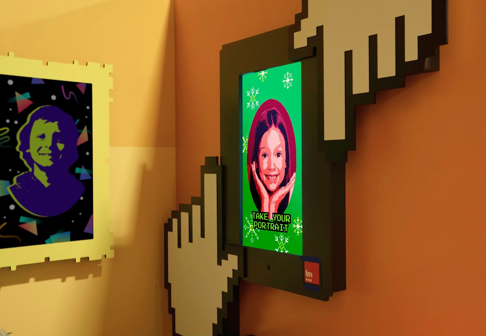 Pixel Portrait station. Giant pixel hands frame a screen that reads Take your portrait, showing a girl redrawn in 8-bit style.